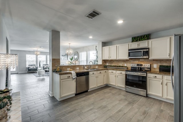 kitchen featuring sink, white cabinets, a chandelier, decorative backsplash, and stainless steel appliances