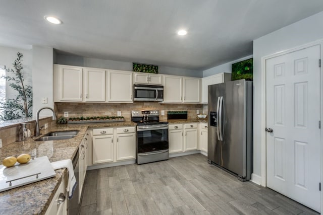 kitchen with appliances with stainless steel finishes, tasteful backsplash, sink, light stone counters, and light hardwood / wood-style flooring