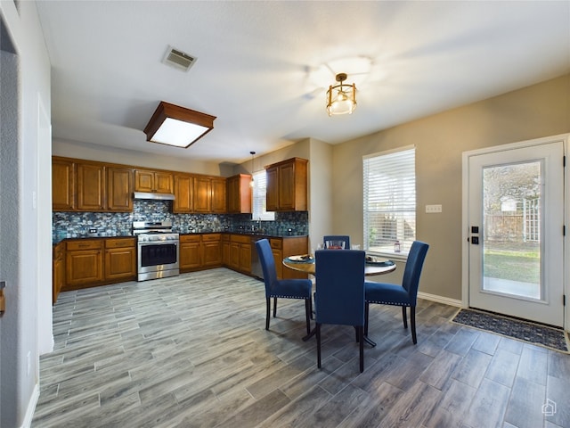 kitchen featuring pendant lighting, stainless steel range with gas stovetop, light wood-type flooring, and decorative backsplash