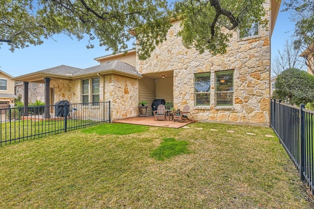 rear view of property with stone siding, a lawn, a patio area, and fence