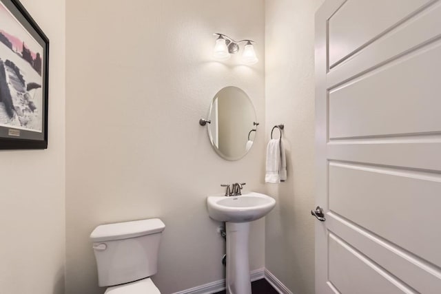 half bath featuring baseboards, a sink, and toilet