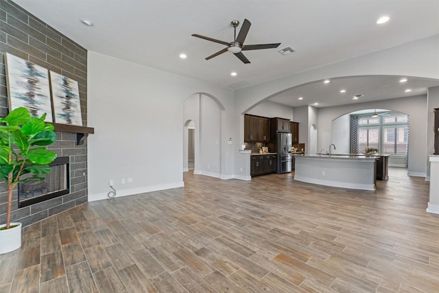 unfurnished living room with sink, light hardwood / wood-style flooring, a large fireplace, and ceiling fan