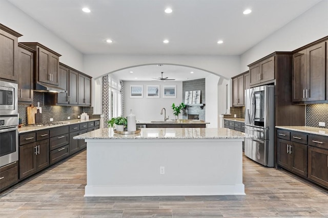 kitchen with light stone counters, dark brown cabinets, appliances with stainless steel finishes, and a kitchen island