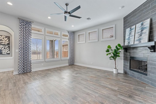 unfurnished living room featuring wood-type flooring, a tile fireplace, and ceiling fan