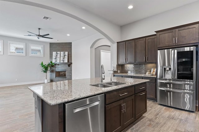 kitchen featuring dark brown cabinetry, sink, appliances with stainless steel finishes, an island with sink, and backsplash