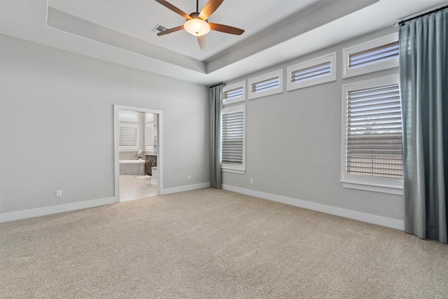 unfurnished bedroom with multiple windows, ensuite bathroom, a raised ceiling, and light carpet