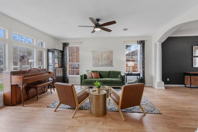 sitting room featuring light wood-type flooring, arched walkways, decorative columns, and ceiling fan