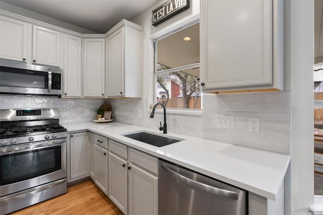 kitchen featuring a sink, light countertops, appliances with stainless steel finishes, light wood finished floors, and tasteful backsplash