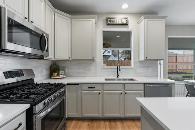 kitchen featuring stainless steel appliances, tasteful backsplash, light countertops, light wood-style floors, and a sink