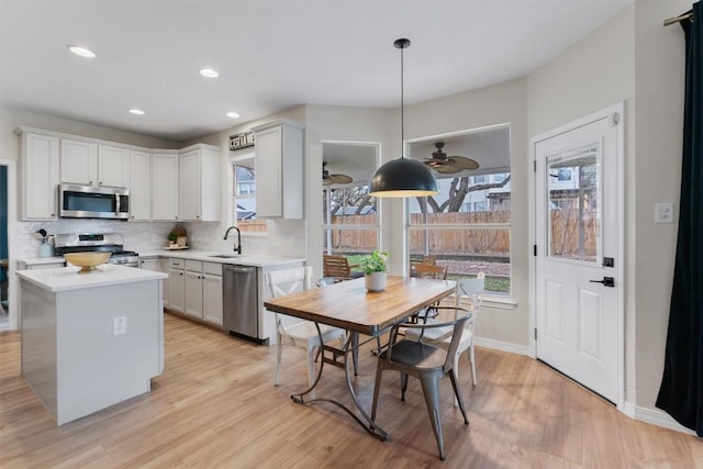 kitchen with stainless steel appliances, a sink, light wood-style floors, light countertops, and tasteful backsplash