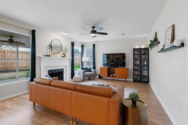 living area with a healthy amount of sunlight, light wood-type flooring, a fireplace, and a ceiling fan