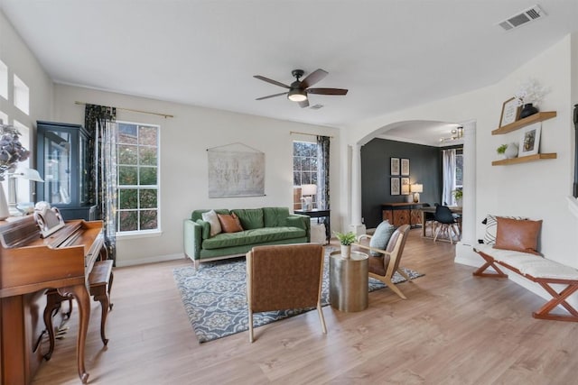 living room with light wood-type flooring, arched walkways, visible vents, and ceiling fan