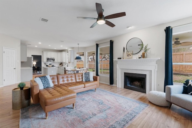 living room featuring a ceiling fan, light wood-type flooring, a fireplace, and recessed lighting