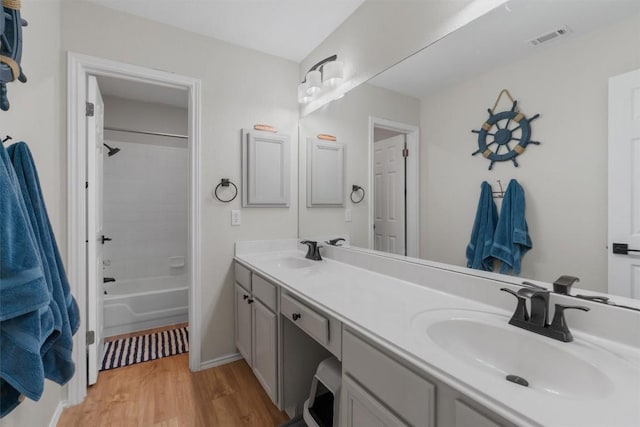 full bath with double vanity, visible vents, a sink, and wood finished floors