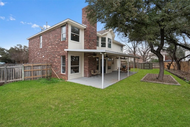 back of house featuring ceiling fan, a fenced backyard, brick siding, a lawn, and a chimney