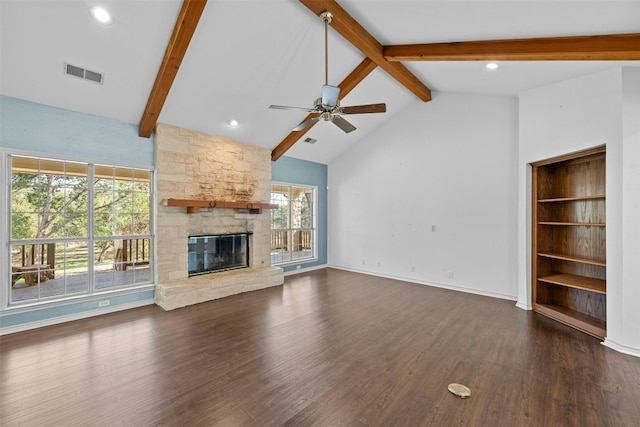 unfurnished living room featuring dark wood-type flooring, ceiling fan, a stone fireplace, and beamed ceiling