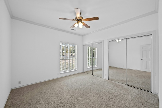 unfurnished bedroom with multiple closets, crown molding, light carpet, and ceiling fan