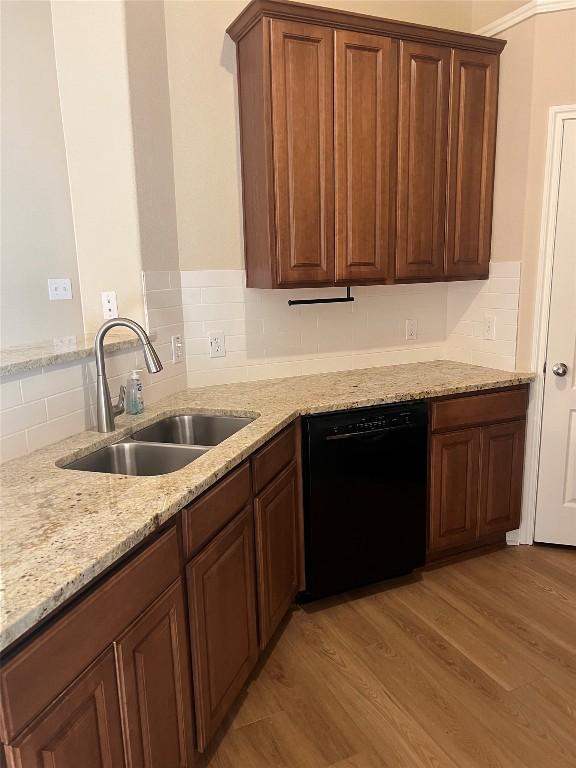 kitchen with sink, black dishwasher, tasteful backsplash, light stone countertops, and light wood-type flooring