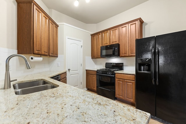 kitchen with sink, tasteful backsplash, light stone countertops, and black appliances