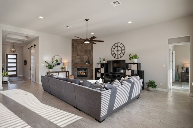 living room featuring a tile fireplace, a barn door, and ceiling fan