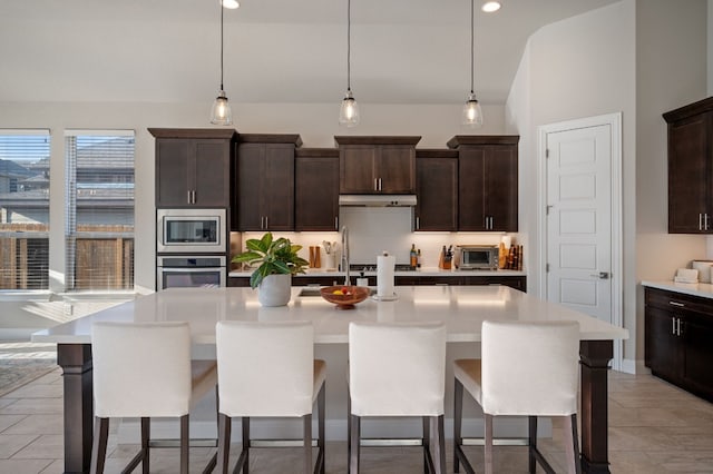 kitchen featuring stainless steel appliances, decorative light fixtures, an island with sink, and dark brown cabinets