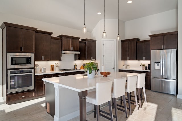 kitchen with dark brown cabinetry, a breakfast bar, a center island with sink, appliances with stainless steel finishes, and pendant lighting