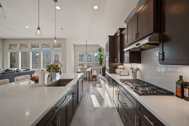 kitchen with sink, hanging light fixtures, dark brown cabinetry, stainless steel appliances, and light stone countertops