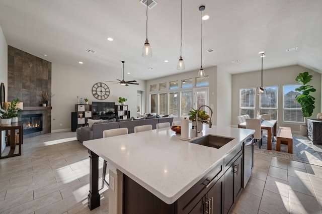 kitchen featuring sink, light stone counters, dark brown cabinets, a tile fireplace, and a kitchen island with sink