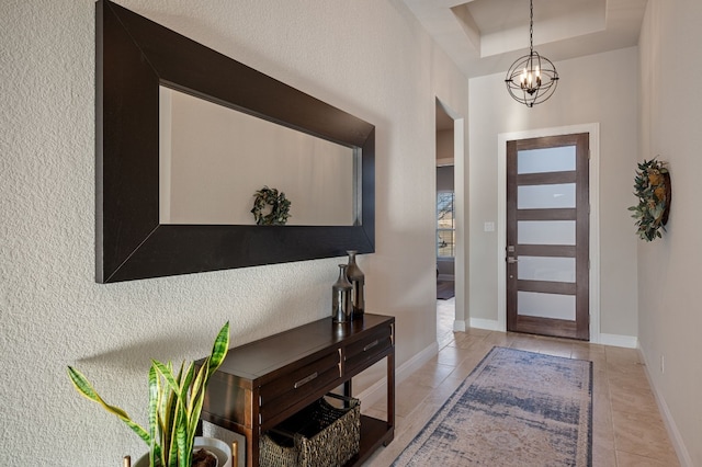 foyer with a raised ceiling, light tile patterned floors, and a chandelier