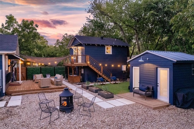 back house at dusk featuring an outdoor living space with a fire pit, a deck, and a storage unit