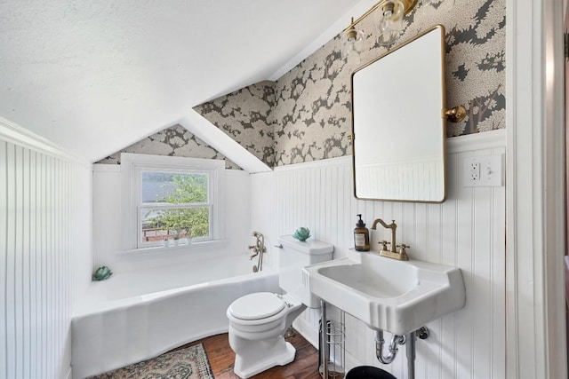 bathroom with vaulted ceiling, hardwood / wood-style floors, sink, a tub to relax in, and toilet