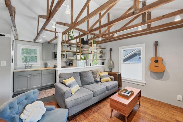 living room with lofted ceiling with beams, sink, and light hardwood / wood-style flooring