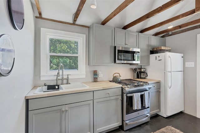 kitchen featuring beamed ceiling, appliances with stainless steel finishes, sink, and gray cabinetry