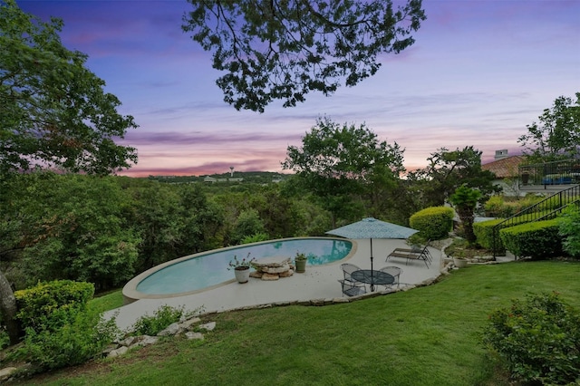 pool at dusk featuring a lawn, a patio area, and an outdoor pool