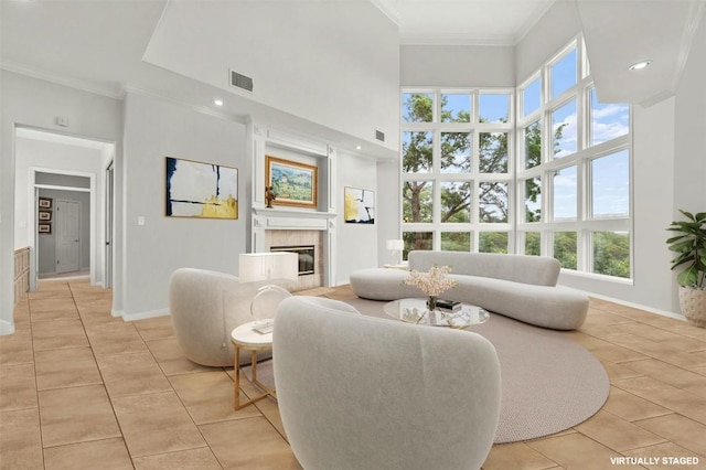 living room featuring light tile patterned flooring, ornamental molding, a tile fireplace, and a high ceiling