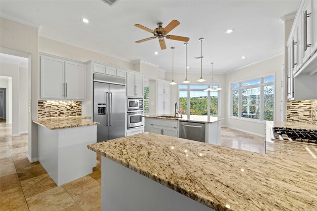 kitchen featuring built in appliances, decorative light fixtures, a kitchen island with sink, and white cabinets