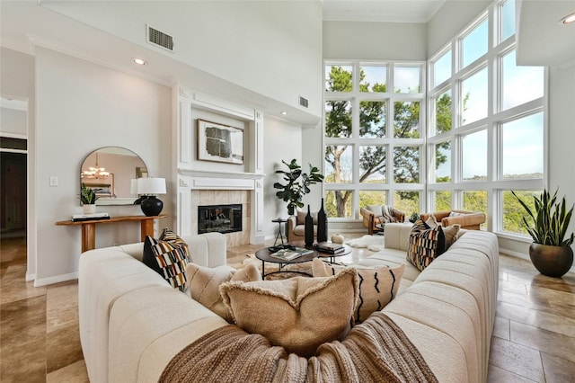 living room with a high ceiling, a fireplace, visible vents, baseboards, and ornamental molding