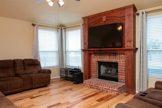 living room featuring ceiling fan, a brick fireplace, and light wood-type flooring