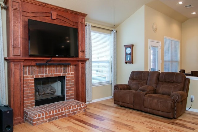 living room featuring a brick fireplace, vaulted ceiling, and light hardwood / wood-style floors