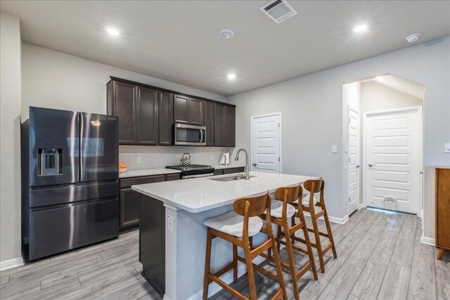 kitchen featuring sink, appliances with stainless steel finishes, a kitchen island with sink, dark brown cabinetry, and light wood-type flooring