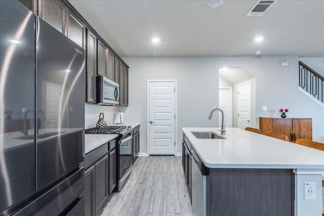 kitchen featuring stainless steel appliances, sink, light hardwood / wood-style floors, and a kitchen island with sink