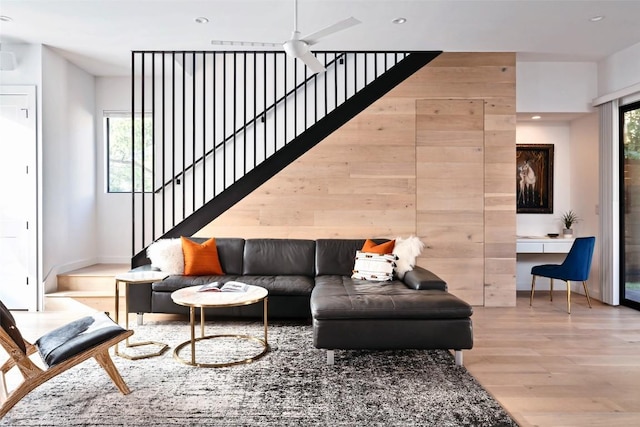 living room with light hardwood / wood-style flooring, wooden walls, ceiling fan, and a high ceiling