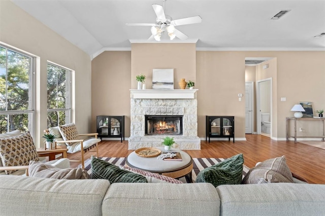 living room with a stone fireplace, vaulted ceiling, ornamental molding, ceiling fan, and light hardwood / wood-style floors