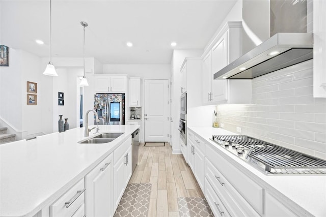 kitchen with decorative light fixtures, white cabinetry, sink, stainless steel appliances, and wall chimney exhaust hood