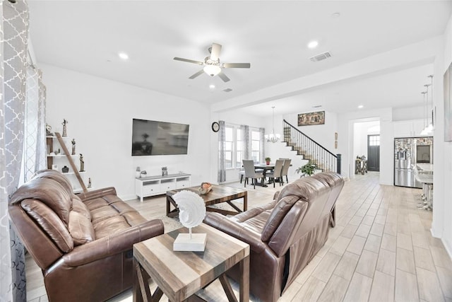 living room featuring ceiling fan with notable chandelier and light hardwood / wood-style flooring