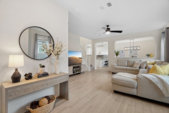 living room with ceiling fan with notable chandelier and light hardwood / wood-style flooring