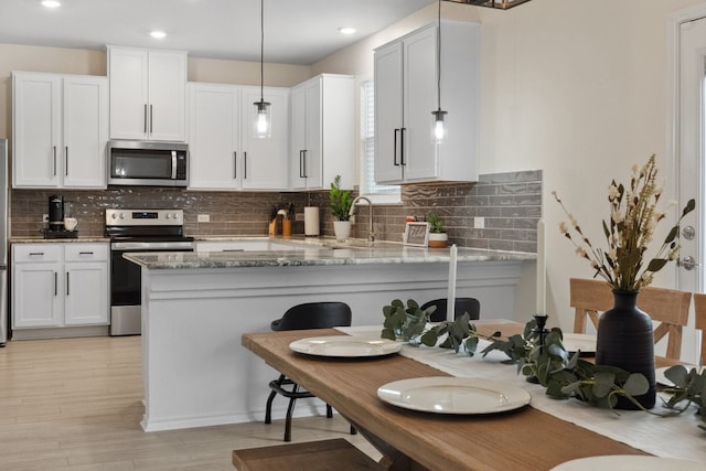 kitchen with white cabinetry, hanging light fixtures, kitchen peninsula, stainless steel appliances, and light stone countertops