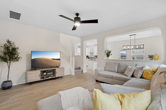 living room with ceiling fan with notable chandelier and light hardwood / wood-style floors