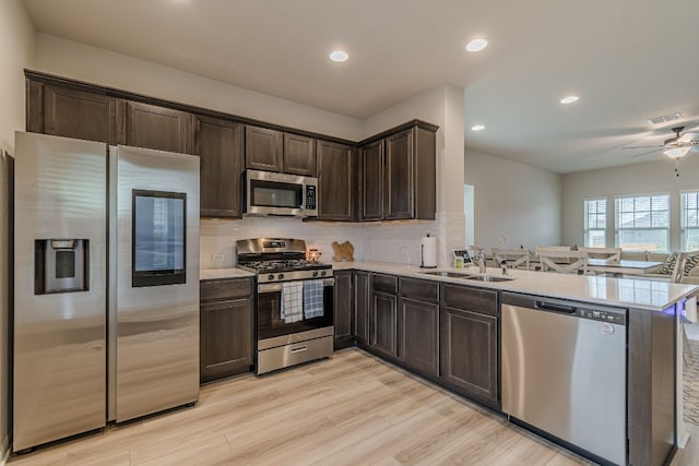 221 Duck Creek Trl, San Marcos, TX 78666 - kitchen with stainless steel appliances, a sink, a peninsula, dark brown cabinets, and decorative backsplash