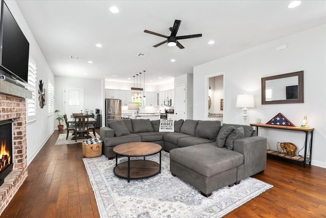 living room featuring baseboards, visible vents, dark wood finished floors, a brick fireplace, and recessed lighting